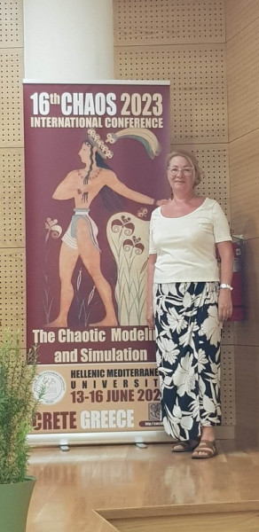 prof. Lidia Dierzbickiej-Głowackiej na tle banneru reklamującego konferencję pt. 16th Chaotic modeling and simulation conference